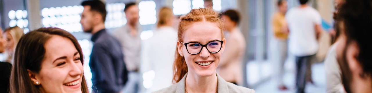 Zwei junge Frauen mit Mappen in der Hand unterhalten sich auf einer Messe mit einem Mann