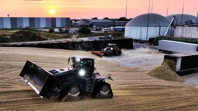 Field with agricultural vehicles and a biogas plant in the background