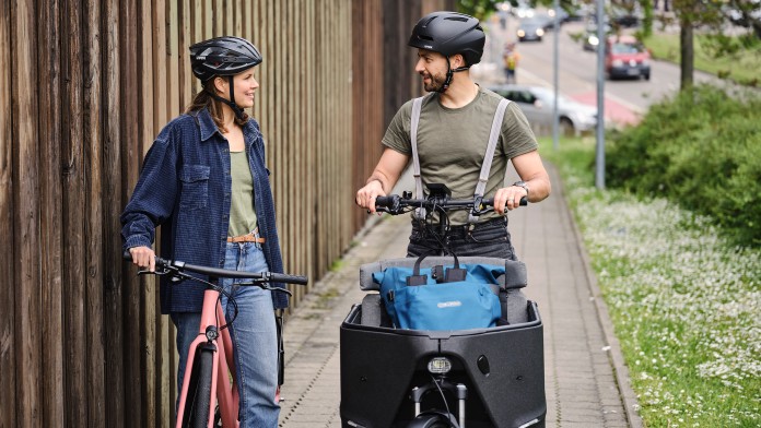 Eine Frau auf einem Fahrrad und ein Mann auf einem Lastenrad unterhalten sich